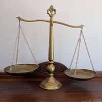 Front view of brass balance scales on a wooden surface, showing full length and details of the beam and pans.