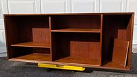 Front view of mid century open wooden cabinet showing three vertical sections divided by shelves. Warm brown color with wood grain detail.