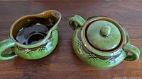 Green glazed pottery creamer and sugar bowl with lid, featuring brown accents and black cross-hatch decoration