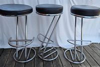 Front view of all three bar stools side by side, showing their round black cushions and chrome tubular metal frames.