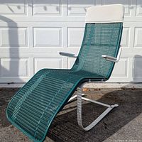 Full view of the outdoor green spring lounger chair showing the white frame, armrests, green woven webbing seat and back, and white headrest.