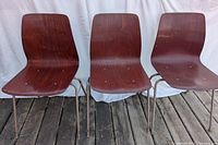 Three dark stained wooden plywood stacking chairs with metal frames standing side by side on wooden floor