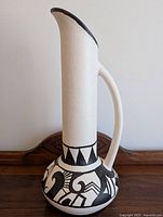 Full view of the tall vase showing white ceramic with a black rim, curved handle, and black tribal patterns at the base.
