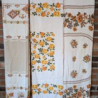 Three vintage cotton tablecloths hung vertically showing floral and geometric patterns