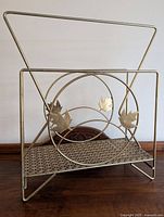 Full view of the metal record rack showing the triangular frame, circular center with maple leaf decorations, and perforated shelf base.