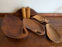 Four vintage wooden serving boards and two wooden salt and pepper mills arranged on a wooden surface, showing size and shape variations.
