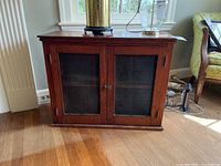 Front view of antique wooden cabinet showing two glass doors with mesh panels and a metal latch lock