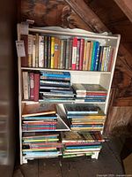 Front view of white wooden bookcase filled with books, showing scalloped top edge and three shelves.