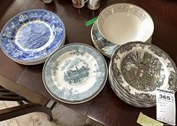 Photo showing multiple plates with distinct historic and scenic blue and brown designs stacked on table.