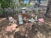 Wide view showing all cement statues and metal duck decor arranged on ground near tree and fence.
