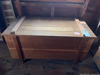 Front view of rectangular wooden chest with reinforced corners and hinged lid, showing wood grain and overall natural finish.