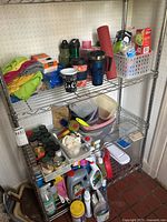 Metal shelving unit with cleaning supplies, water bottles, travel mugs, kitchen cloths, and food containers organized across three shelves