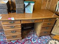 Front view of wooden desk showing central drawer and six side drawers with ornate metal handles, sitting on a patterned carpet.