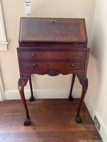 Front view of vintage drop front secretary desk showing two drawers, drop front writing surface with lock, carved details, and claw foot legs.