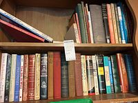 Shelf with assortment of hardcover books showing varieties of titles and conditions.