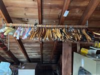 Full view of wooden, metal and padded hangers hanging on wooden rack under sloped wooden ceiling.