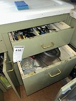 Open lower kitchen drawer containing glass and plastic food storage containers with lids, also showing open cupboard door beneath the drawer