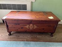 Front view shows Lane cedar chest with decorative metal lock plate, keyhole, turned wooden legs, and overall wood grain finish.