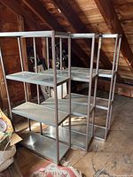Three metal shelving units placed in an attic space with wood floor and exposed rafters visible.