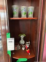 Four frosted glasses with floral designs on top shelf, and various miniatures and art glass vase on shelf below