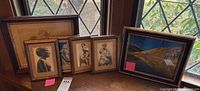Five framed prints grouped by window showing a mix of black and white figurative prints and one color landscape.