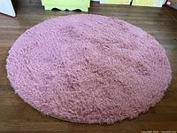 Full view of round pink shag rug on wooden floor.