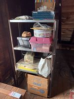 Shelf with assorted storage containers, cardboard boxes, sewing box and a pink plastic bin visible