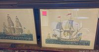 Two framed prints depicting different sailing ships with sails and flags, framed in brown wood and measuring about 21x27 inches each.