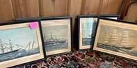 View of nine framed ship prints grouped together on a carpeted floor showing varied sailing ships in black frames.