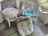 White painted wicker chair with turquoise cushion and matching round wicker table in a corner of a porch.
