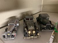 Three vintage style toy cars placed on a shelf, showing front and side views; dusty surfaces visible