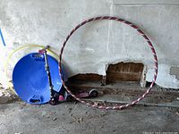 Photo showing all items together: two hula hoops leaning against a wall, blue snow saucer sled, and pink/black scooter.