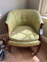 Front angled view of the vintage green floral accent chair showing its curved backrest, wooden arms, and cushion seat with visible wear.