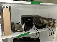 Several vintage clocks, radios and camera on a white shelf including Seth Thomas clock, Seiko clock, Kodak camera, Juliette radio, Sony clock radio cassette.