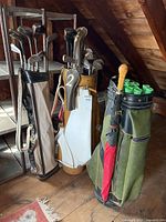 Wide view showing three vintage golf bags on wooden floor, each with multiple golf clubs including irons and woods