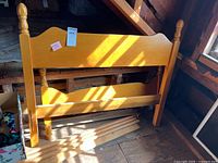 Photo showing the wooden headboard with turned posts and wooden side rails plus support slats laid on the floor.