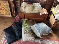 Overview showing Wool duvet, leather bag, several folded blankets and throws on floor near wooden chest.