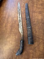 Full view of the antique knife and matching wooden sheath with metal bands on a brown surface.