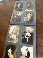 View of a gray antique photo album open to pages with multiple black and white portraits of women and children in formal poses.