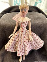 Full-length image of the 16 inch Ashton Drake Collection Gene Incognito doll seated, showing floral dress and gloves.