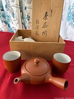 Full set of ceramic teapot, two cups, and wooden box with lid containing Asian script and divider inside.