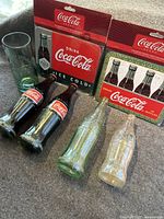 Full lot displaying two Coca-Cola metal trivets, one glass, and four vintage bottles