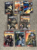 Top view of two sealed G.I. Joe 25th Anniversary comic packs with action figures and six G.I. Joe 25th Anniversary comic books laid out on carpet.