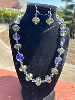 Photo of vintage iridescent glass bead necklace with matching earrings on black display stand outdoors in sunlight.