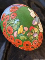 Top and side view of handpainted ceramic Easter egg container showing rabbit, chick, flowers, and decorative stripes.