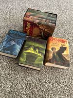 Full set of seven Harry Potter hardcover books with dust jackets laid out on carpet, three books separated showing covers, four books inside original illustrated slipcase.