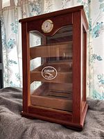 Full view of wooden and glass humidor with three display trays inside and front humidity gauge.