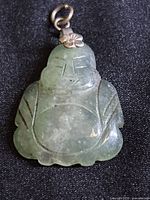 Front view of green jade Buddha pendant carved with facial and body details, showing the metal top with floral decoration and hanging loop.