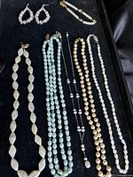 Full view of all 7 pearl jewelry pieces in a tray showing earrings and six necklaces in various pearl colors and shapes.