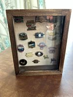 Front view of wooden display box showing 16 mounted motorcycle run pins, including various Harley Davidson designs and skull motifs.